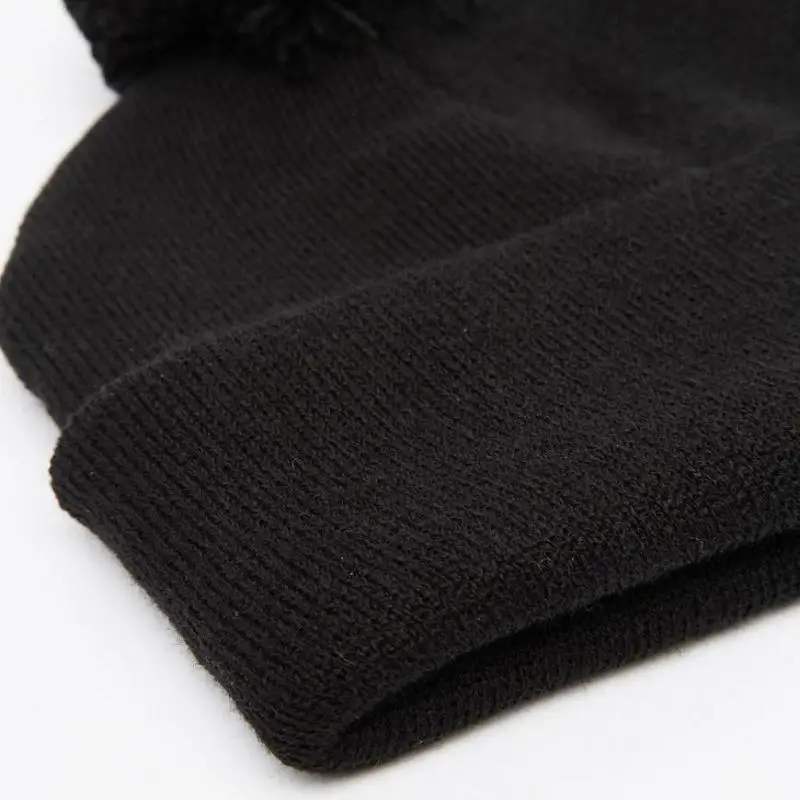 Close-up of a soft, black knit beanie with a folded hat and a pom-pom on top, set against a white background.