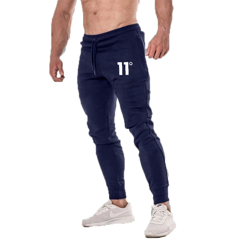 A muscular man in navy blue joggers with "11°" printed on the thigh, wearing white sneakers, posed confidently.