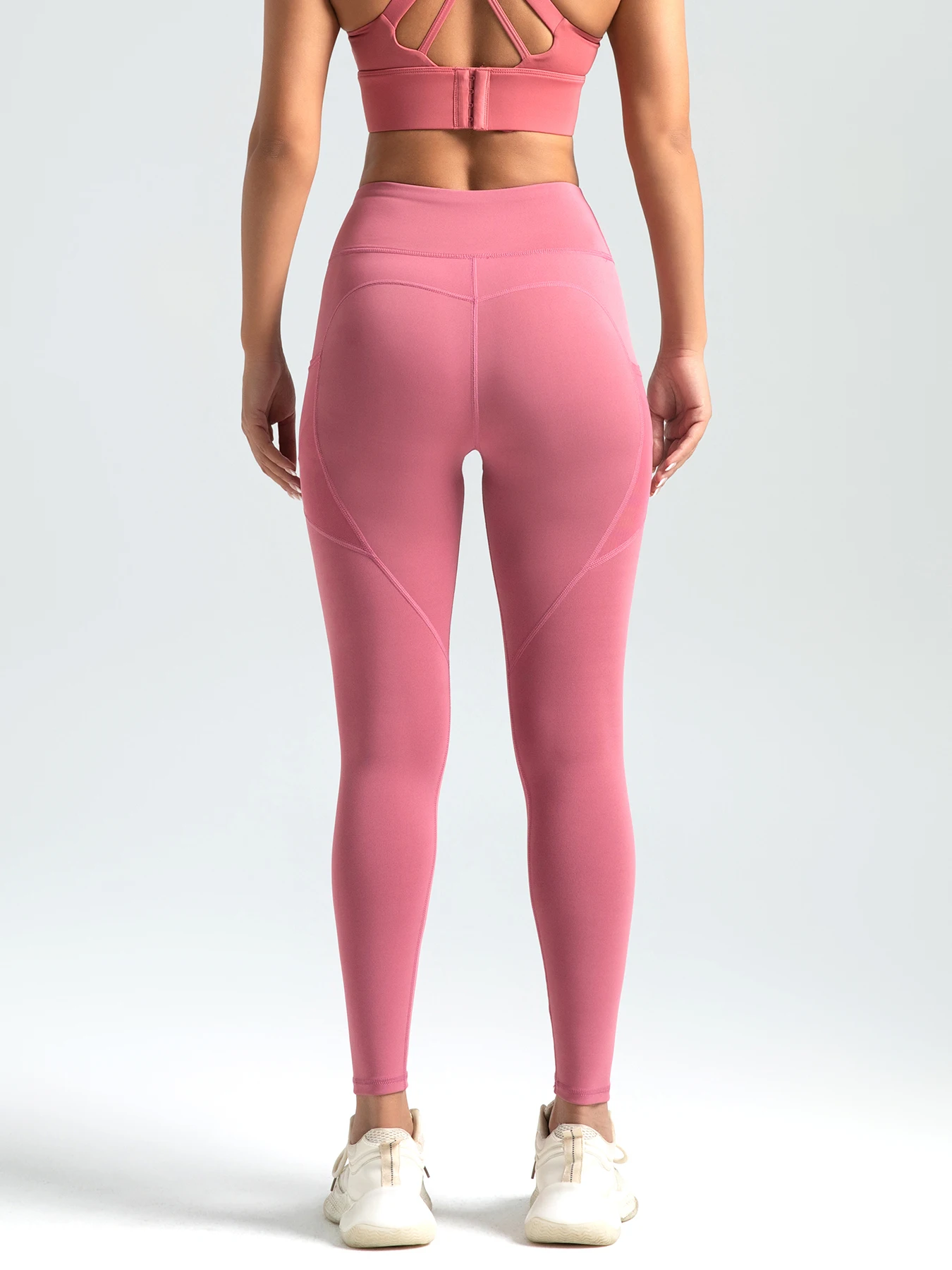 A woman in a pink sports bra and matching leggings stands with her back to the camera, showcasing the athletic outfit.