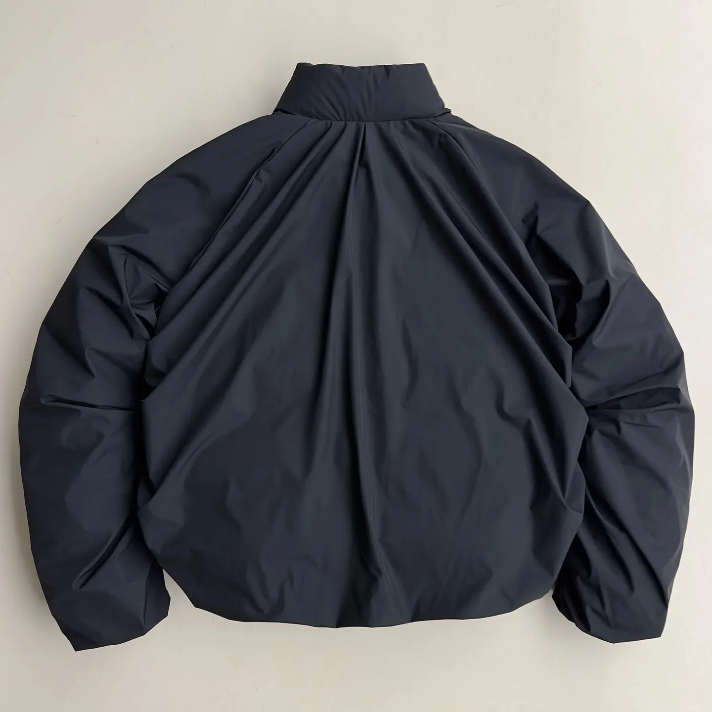 A dark navy puffer jacket viewed from the back, displaying a gathered design and high collar.