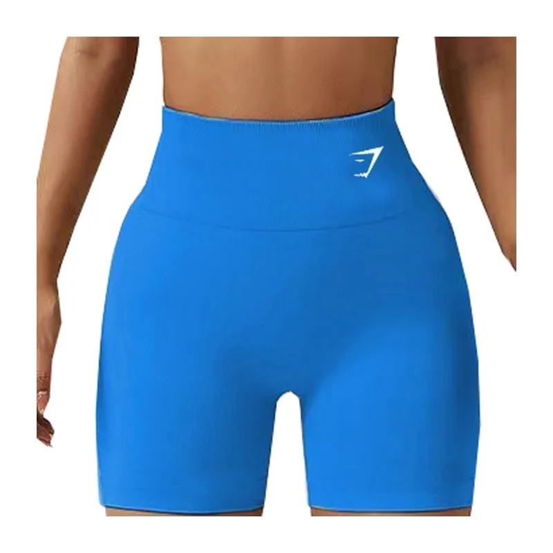 A woman stands wearing high-waisted blue shorts with a small logo on the waistband, showcasing a sleek and sporty design.